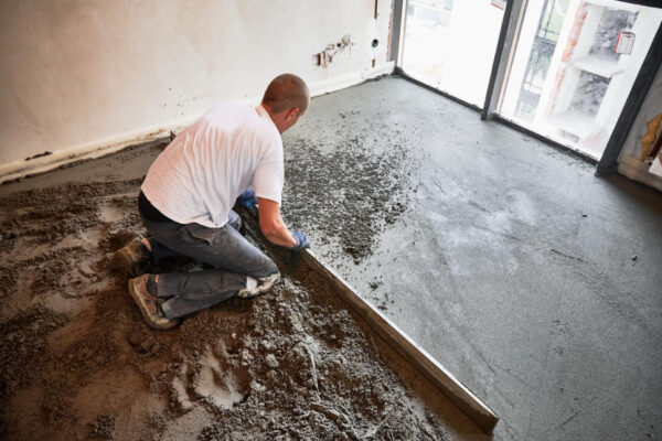 Muncitor nivelează șapă de beton proaspăt turnată